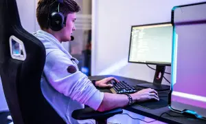 Ein junger Mann mit Headset spielt am PC. Er fragt sich vielleicht, was bedeutet gg im Chat.
