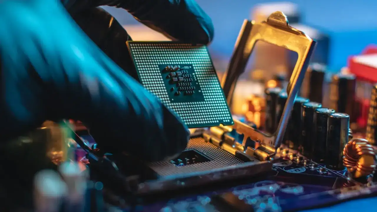 Ein Handschuh hält eine CPU über einen Sockel auf einer Hauptplatine. Ein CPU-Vergleich steht bevor, um die beste Leistung zu ermitteln.