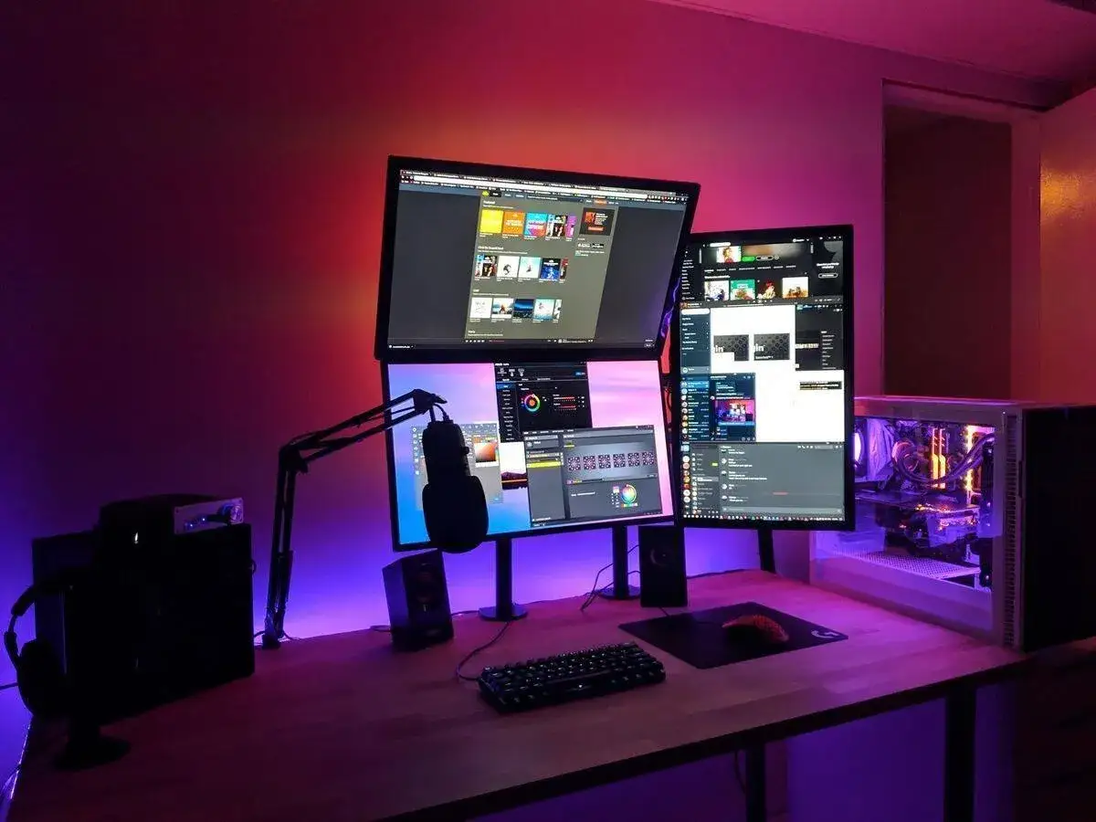 Ein Gaming-Setup mit drei Monitoren, Mikrofon und PC, bereit für kick streaming. Die Beleuchtung ist in Lila und Rot gehalten.